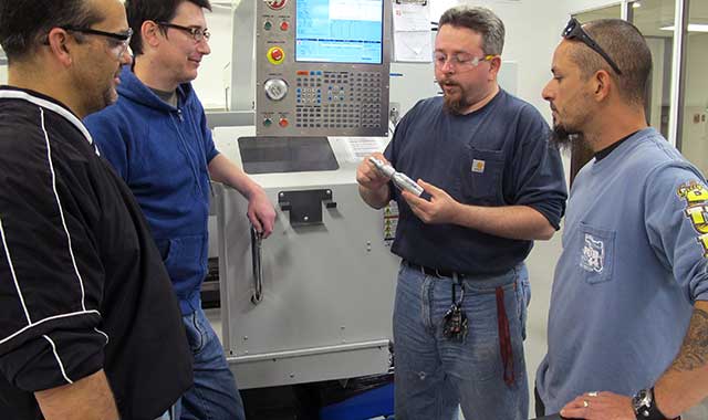 Andy Patterson, Todd Lasco, Jerry Miller and Hector Ortega review how to turn a part in a computerized lathe. Miller, an instructor at McHenry County College, is holding the final piece that students will create during their semester.
